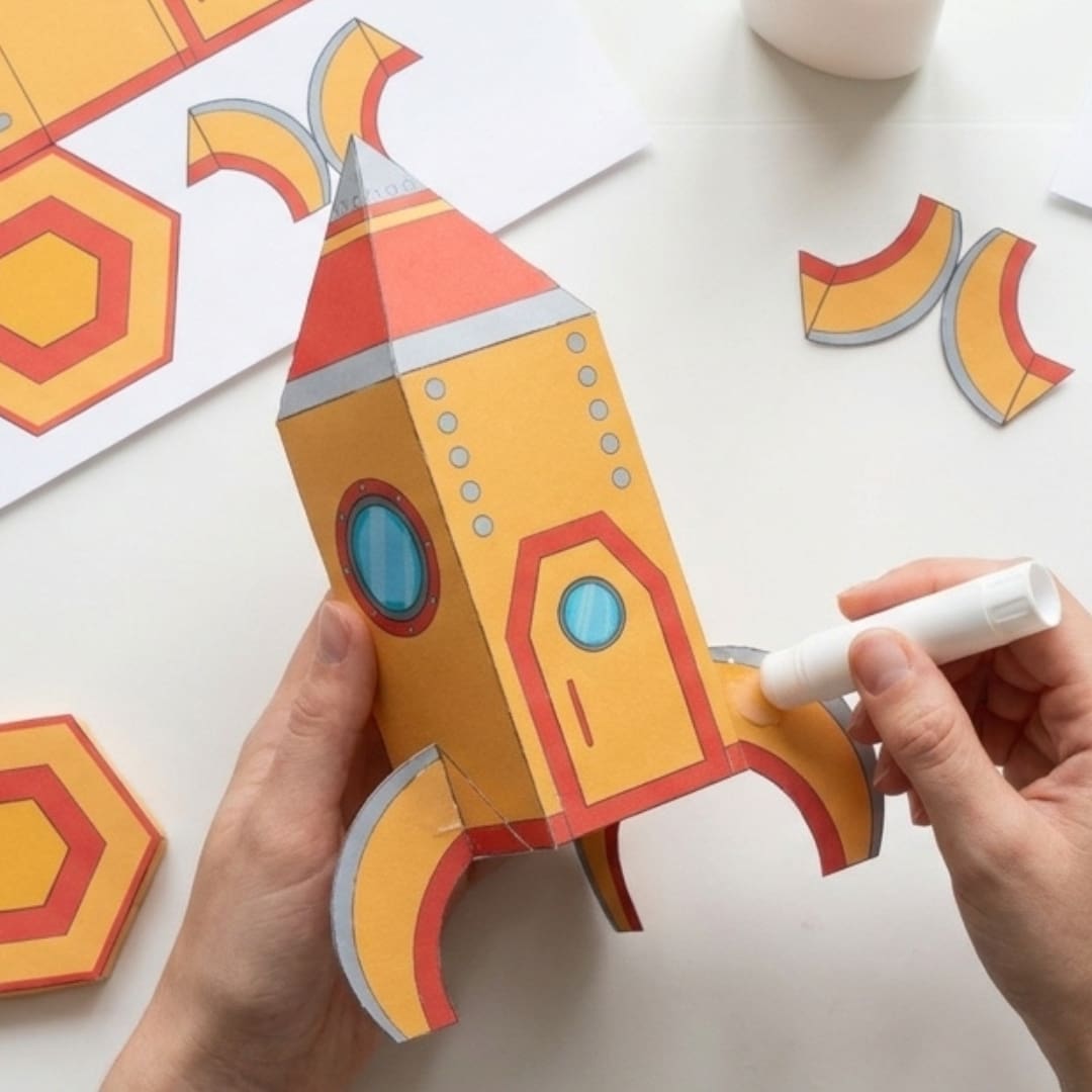 Colorful printable rocket craft template with cut-and-fold parts, including rocket body, nose cone, windows, and boosters, designed as a fun DIY kids activity for easy home or classroom assembly.