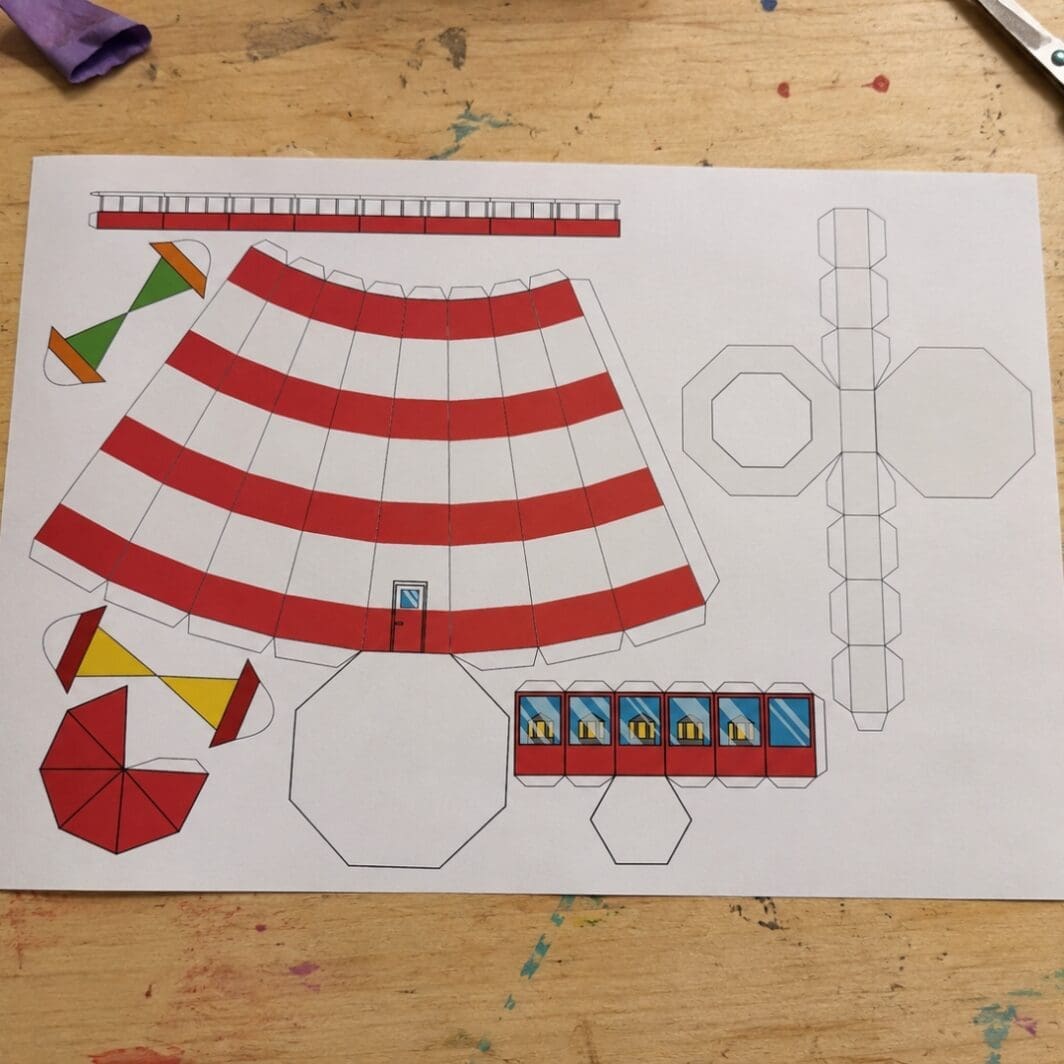 Printable Build a Lighthouse craft sheet placed on a wooden kids’ workshop table with scissors, glue, colored pencils, and craft supplies around it.